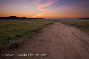 Soft hues blanket the sky at sunset over a road which weaves throughout the farmland in the Big Muddy Badlands in Southern Saskatchewan, Canada.