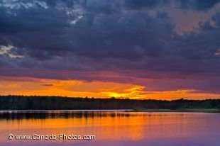 The clouds darken over the St. Mary's River in Sherbrooke, Nova Scotia in Canada but not enough to block out the vibrant sunset colors which highlight the sky.